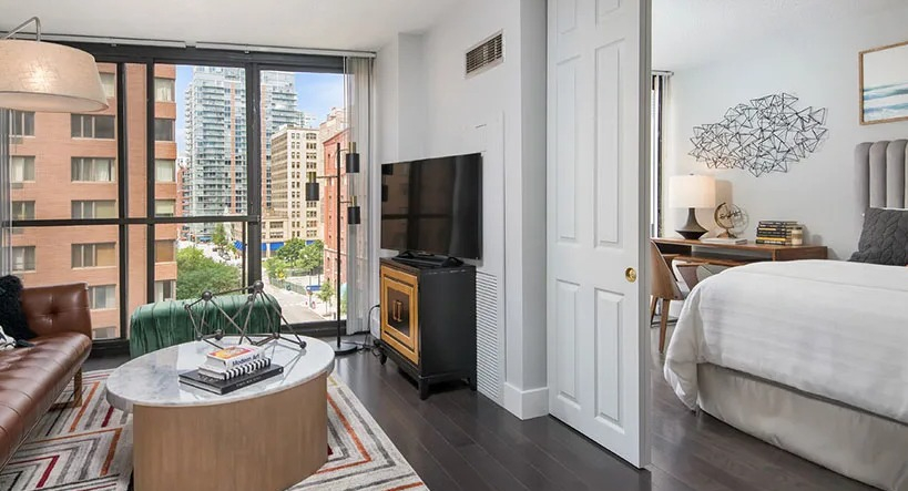 Chic den and bedroom suite with brown leather sofa, sliding doors, and city views at 777 South State apartments in Chicago