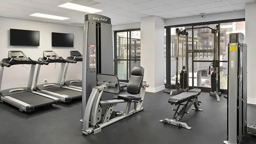 Modern fitness center with treadmills, strength machines, benches, and floor-to-ceiling windows at 777 South State apartments in Chicago