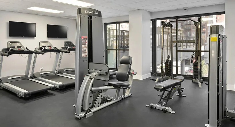 Modern fitness center with treadmills, strength machines, benches, and floor-to-ceiling windows at 777 South State apartments in Chicago