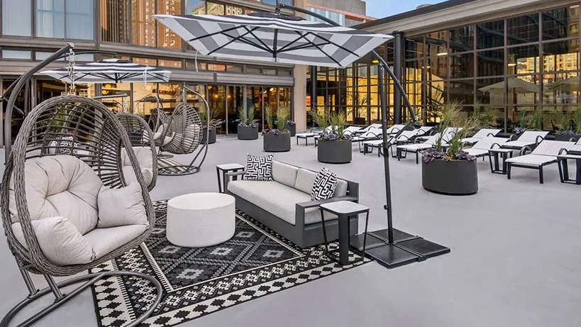 Relaxing outdoor lounge with hanging basket chairs, cushioned seating, and umbrellas on the terrace at 777 South State apartments in Chicago