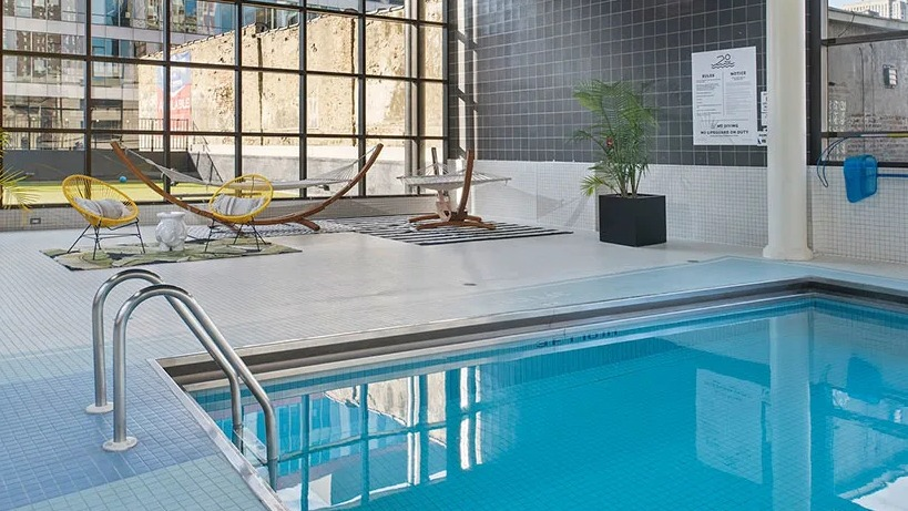 Indoor pool with lounge deck, hammocks, tall industrial windows, and palm accents at 777 South State apartments in Chicago