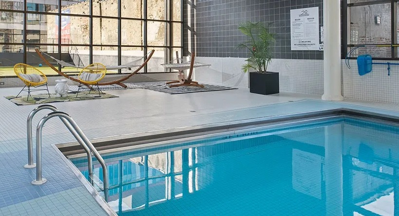 Indoor pool with lounge deck, hammocks, tall industrial windows, and palm accents at 777 South State apartments in Chicago