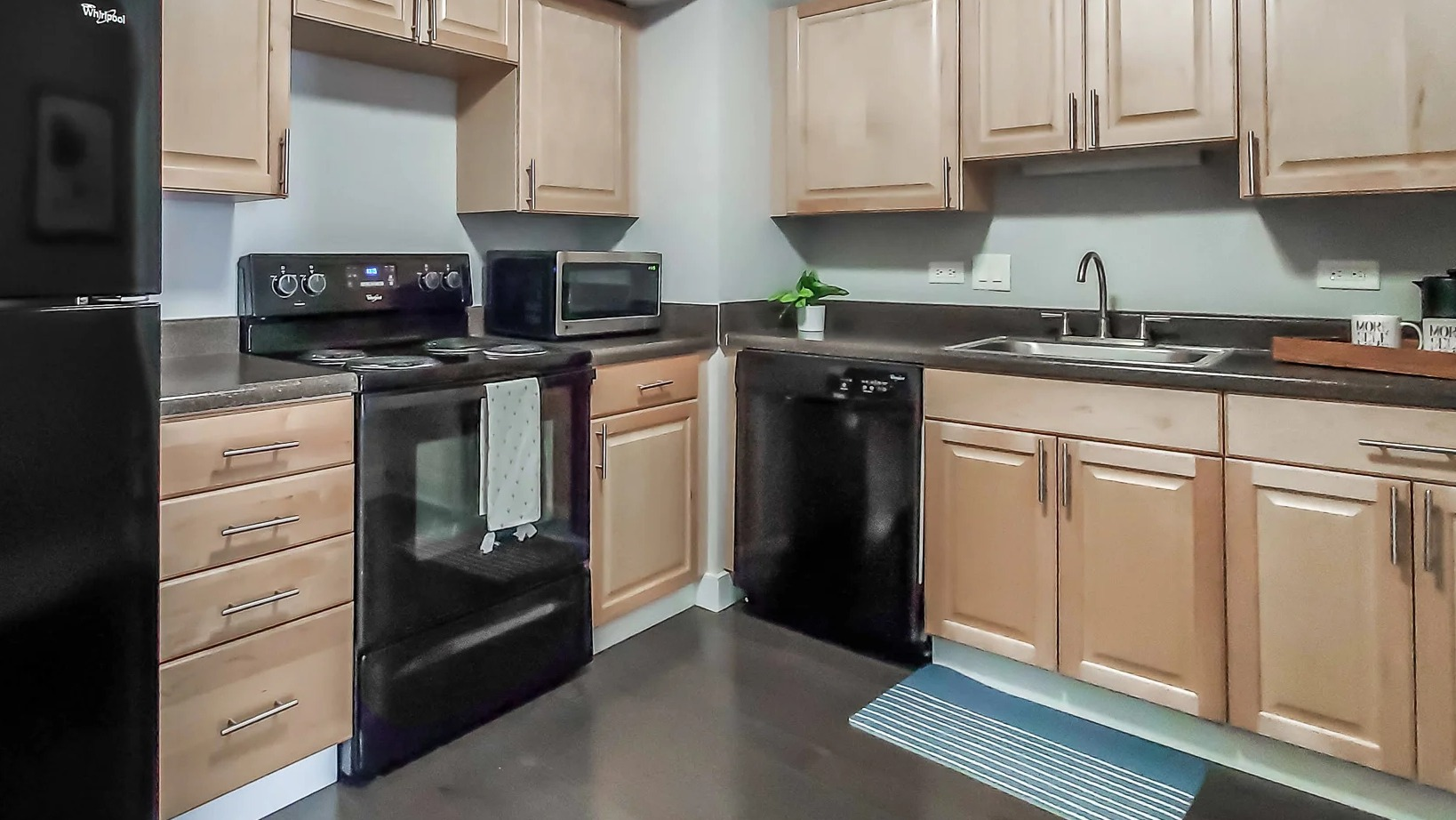 Practical kitchen with light wood cabinetry, black appliances, and ample counter space at 777 South State apartments in Chicago