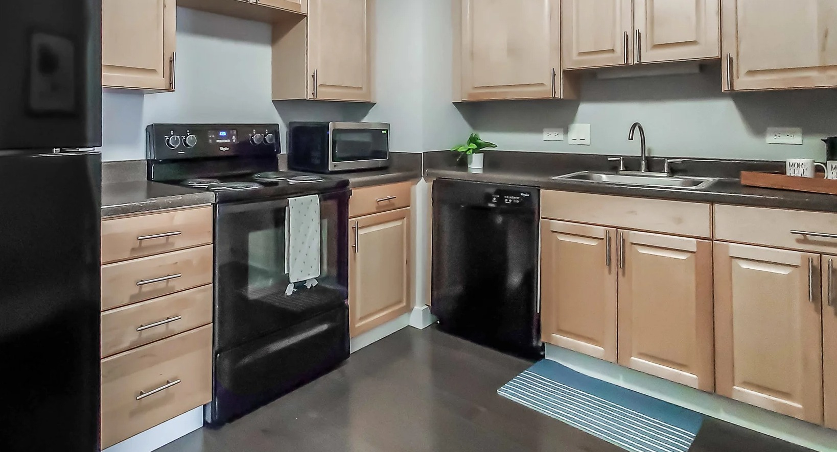 Practical kitchen with light wood cabinetry, black appliances, and ample counter space at 777 South State apartments in Chicago