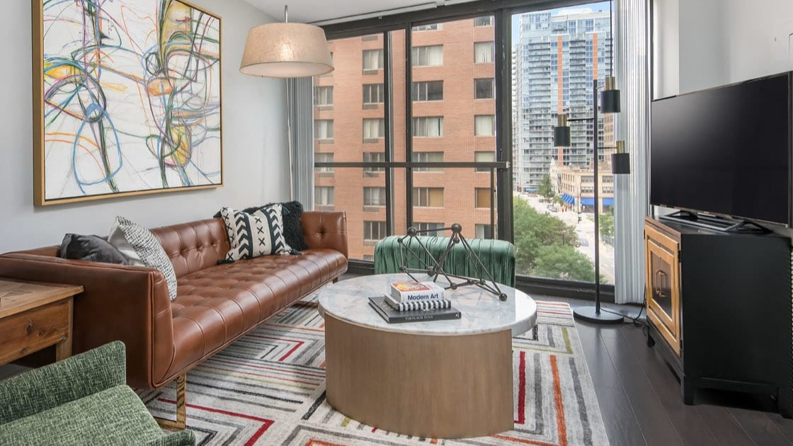 Stylish living room with tufted leather sofa, marble coffee table, and bold geometric rug at 777 South State apartments in Chicago