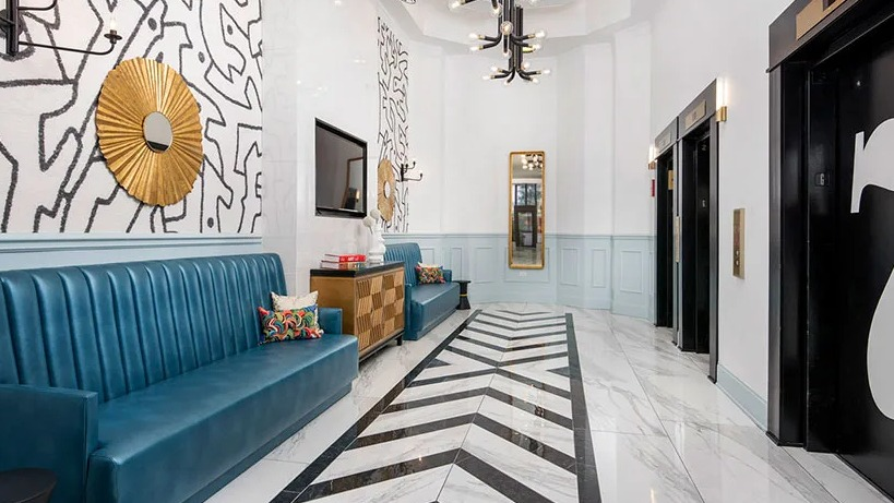 Stylish lobby corridor with teal banquette seating, graphic wall art, and elevators with chevron marble floors at 777 South State in Chicago