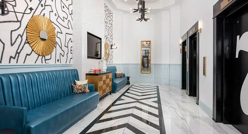 Stylish lobby corridor with teal banquette seating, graphic wall art, and elevators with chevron marble floors at 777 South State in Chicago