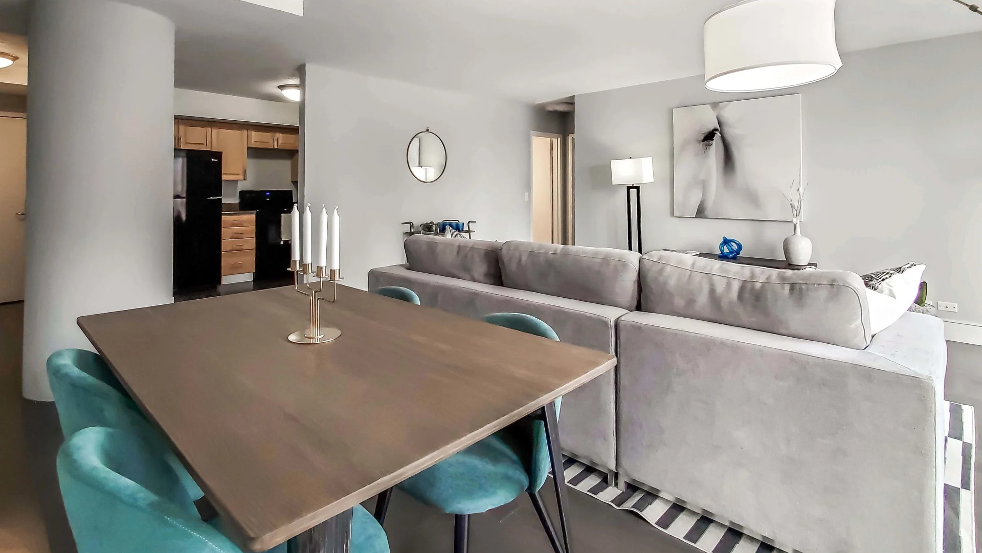 Open living and dining area with teal chairs, gray sectional, and modern lighting near the kitchen at 777 South State apartments in Chicago
