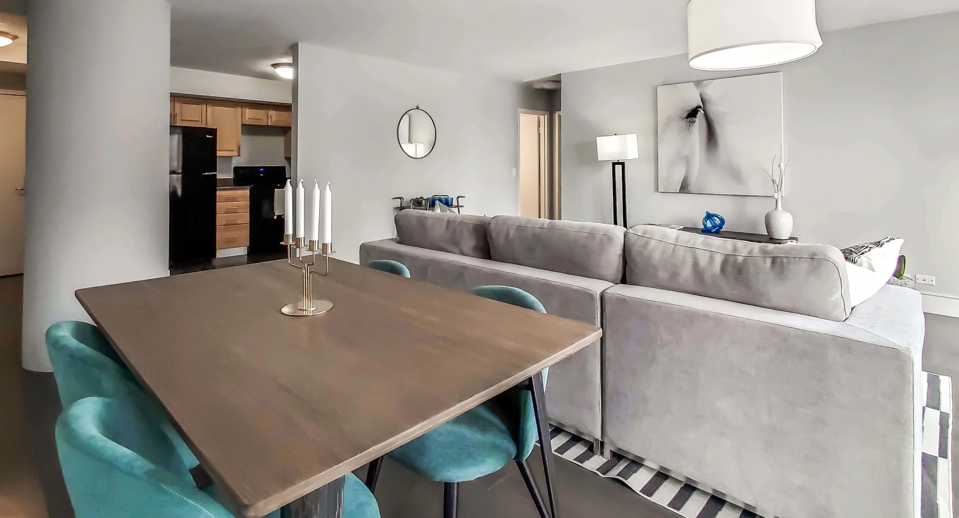 Open living and dining area with teal chairs, gray sectional, and modern lighting near the kitchen at 777 South State apartments in Chicago