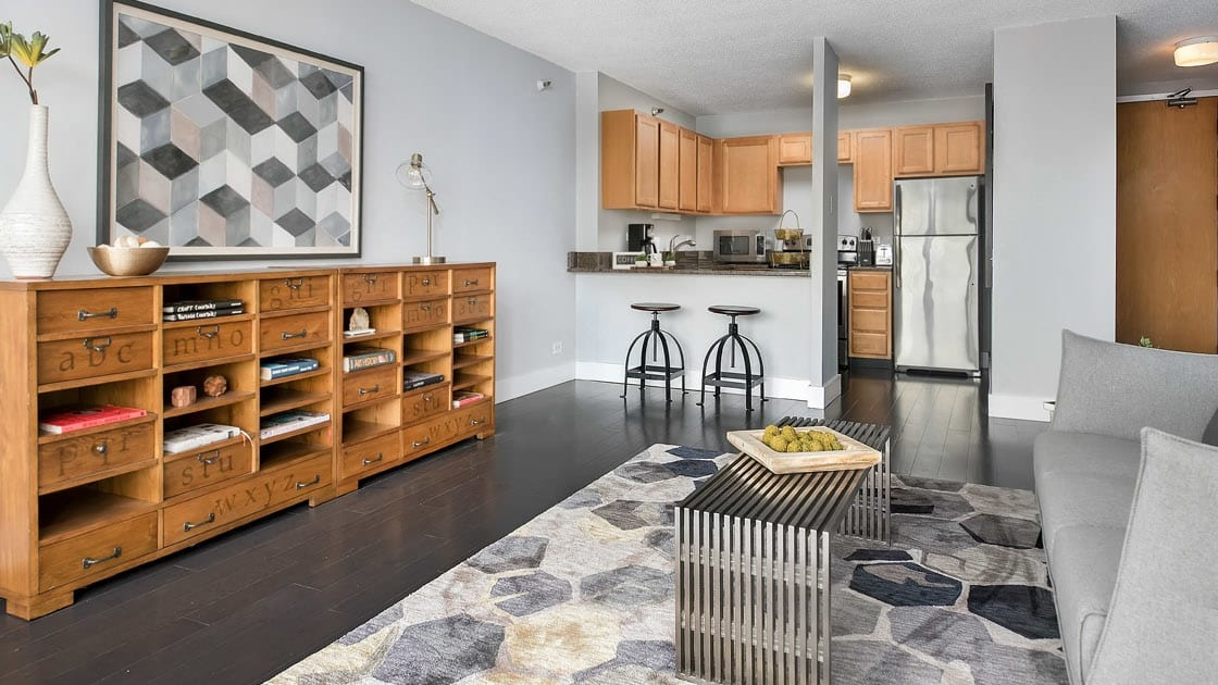Open-concept living area with eclectic rug, modern gray sofa, and breakfast bar kitchen at 777 South State apartments in Chicago
