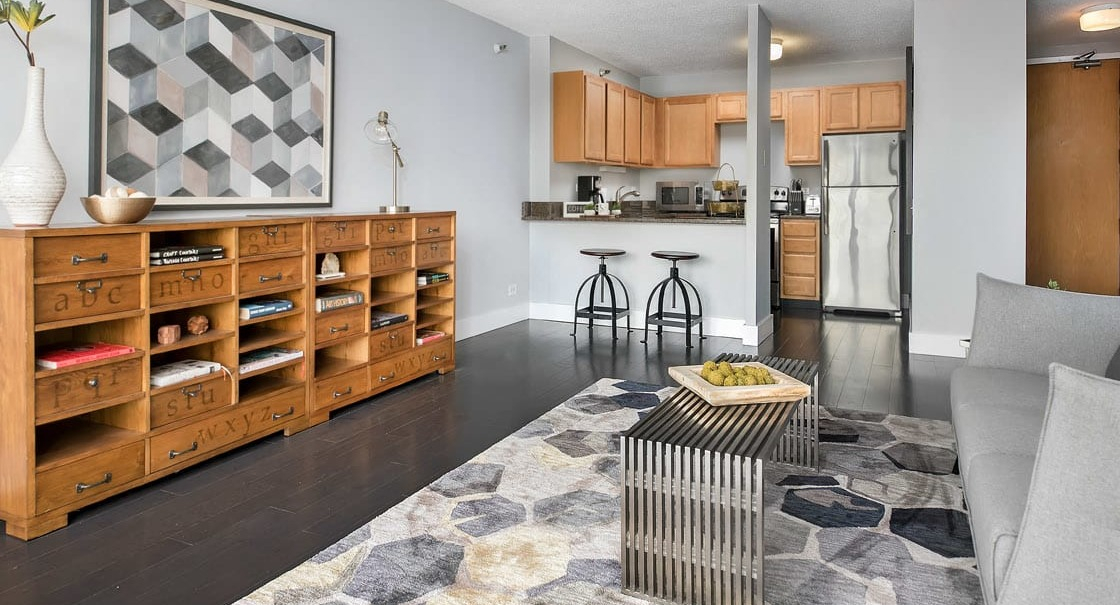 Open-concept living area with eclectic rug, modern gray sofa, and breakfast bar kitchen at 777 South State apartments in Chicago