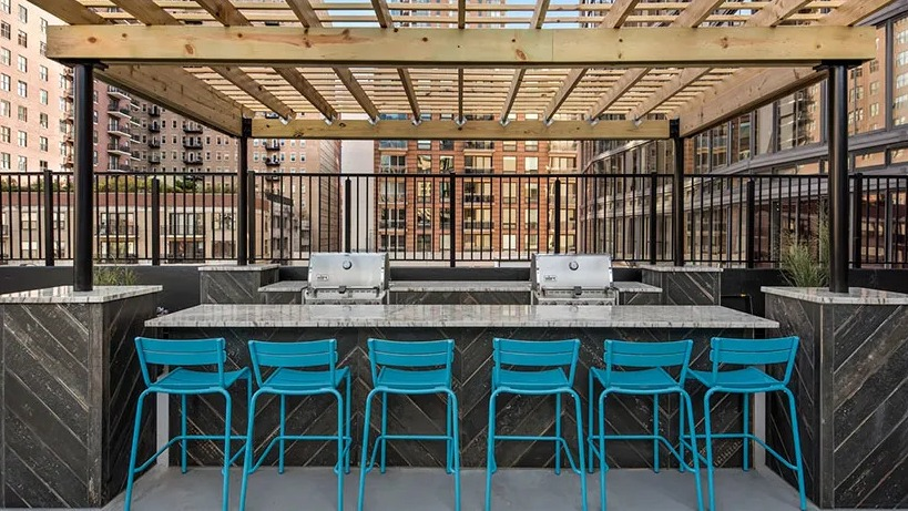 Rooftop grilling station with pergola, bar seating, and stainless grills overlooking the South Loop at 777 South State apartments in Chicago
