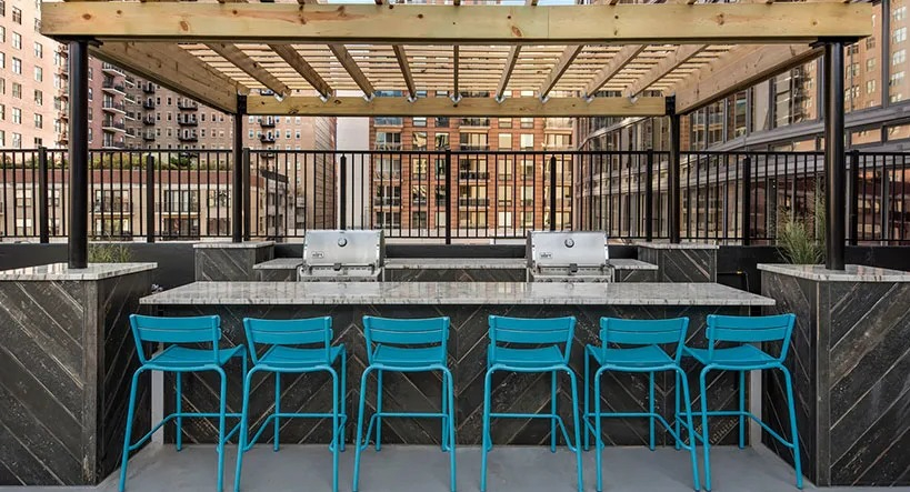 Rooftop grilling station with pergola, bar seating, and stainless grills overlooking the South Loop at 777 South State apartments in Chicago