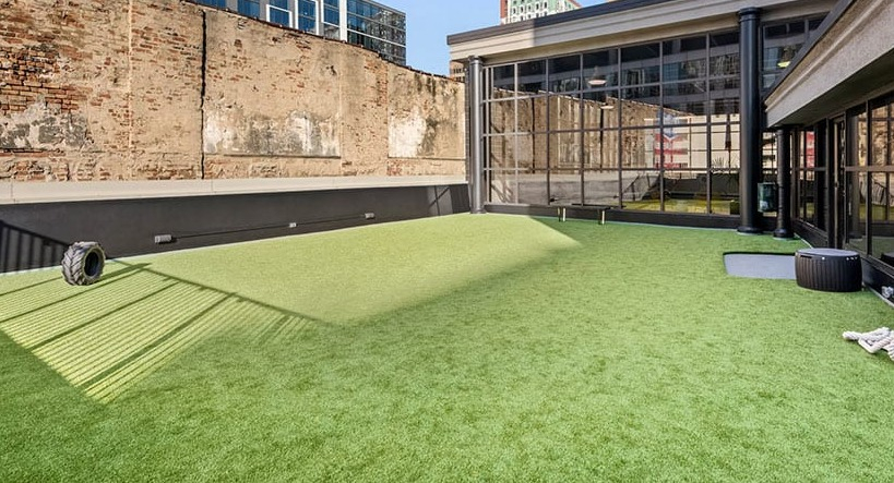 Rooftop turf fitness lawn for bootcamps and outdoor workouts beside glass-walled amenity spaces at 777 South State apartments in Chicago