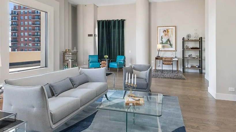Spacious living room with high ceilings, glass coffee table, and large windows overlooking the city at 777 South State apartments in Chicago