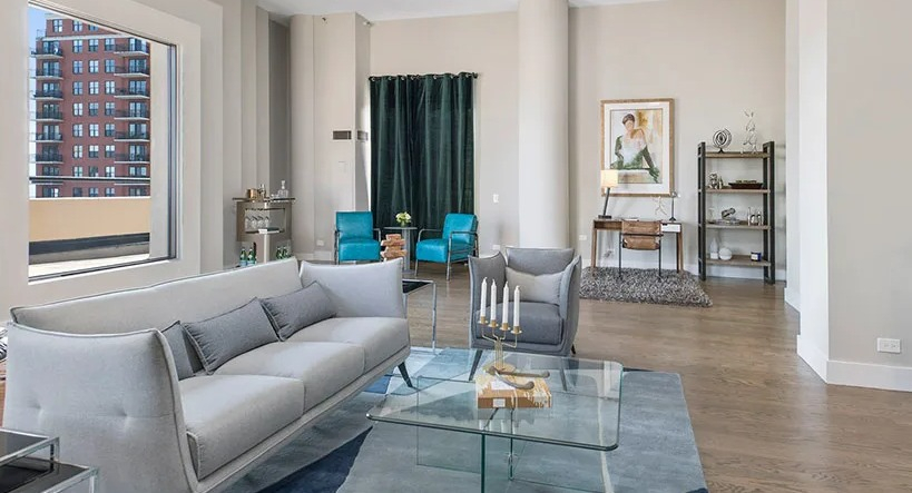 Spacious living room with high ceilings, glass coffee table, and large windows overlooking the city at 777 South State apartments in Chicago
