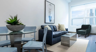 Cozy living and dining nook with blue sofa, glass round table, accent chair, and big windows at 820 Michigan apartments in Chicago
