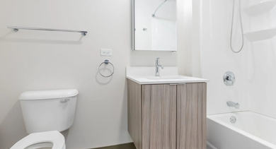 Bright modern bathroom with floating vanity, wide mirror, and shower-tub combo at 820 Michigan apartments in Chicago