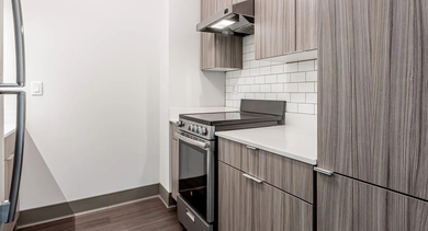 Sleek galley kitchen with wood-grain cabinets, white counters, stainless steel range, and subway tile backsplash at 820 Michigan apartments in Chicago