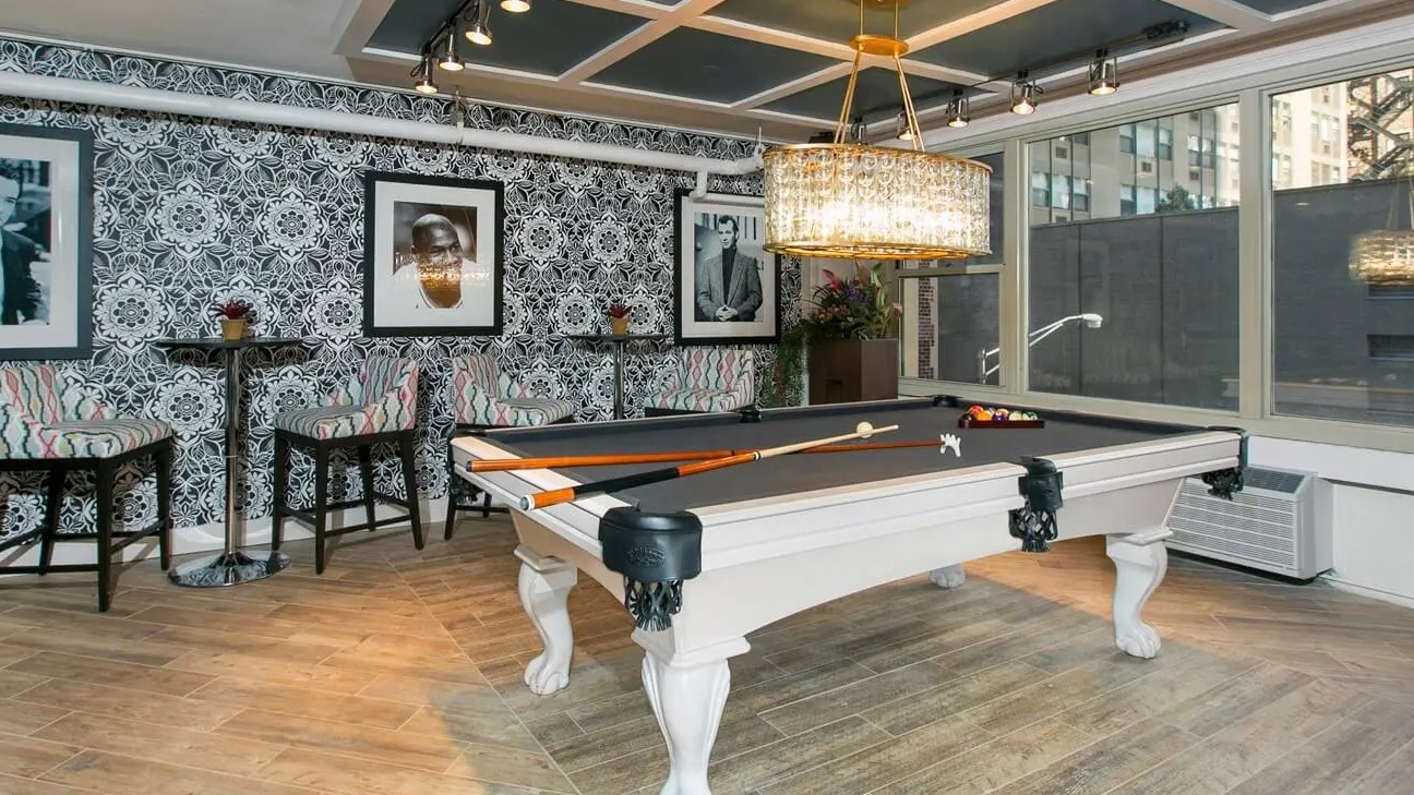 Billiards room with a classic pool table, crystal chandelier, patterned wallpaper, and cafe seating at 860 N Dewitt Apartments in Chicago