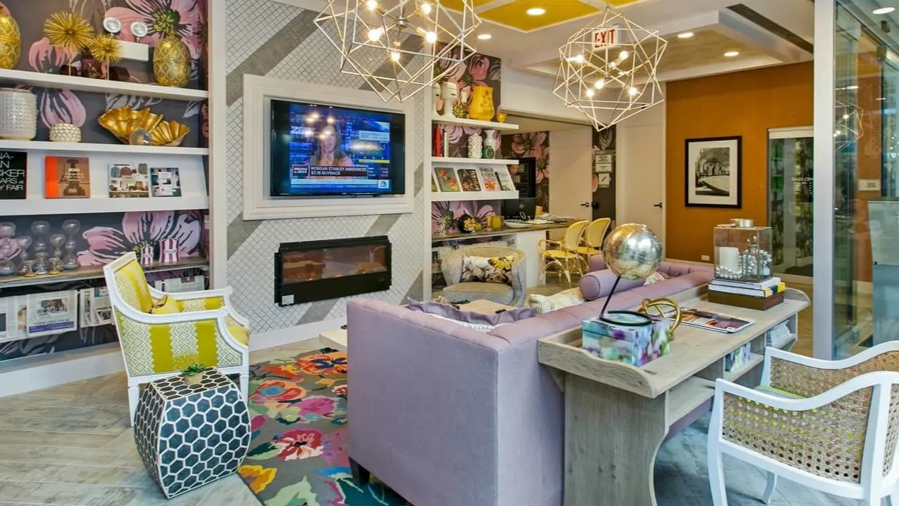 Colorful resident lounge with floral wallpaper, bold yellow ceiling, geometric chandeliers, TV, and fireplace at 860 N Dewitt Apartments in Chicago
