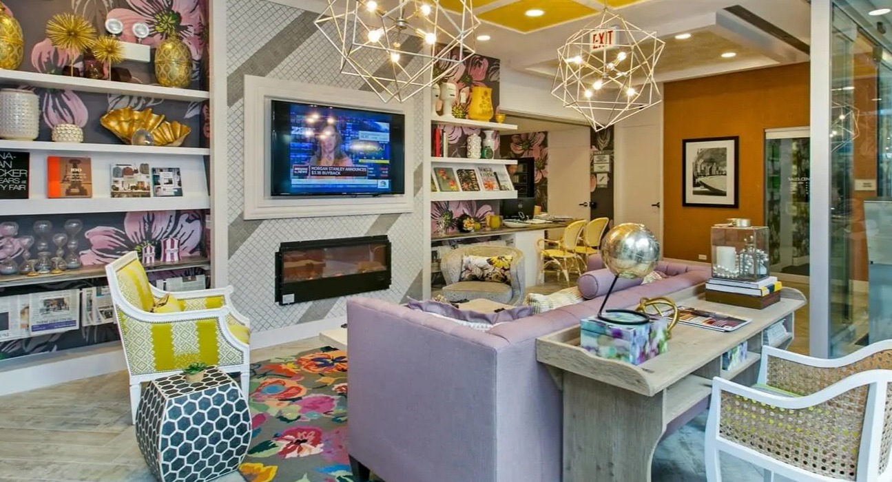 Colorful resident lounge with floral wallpaper, bold yellow ceiling, geometric chandeliers, TV, and fireplace at 860 N Dewitt Apartments in Chicago