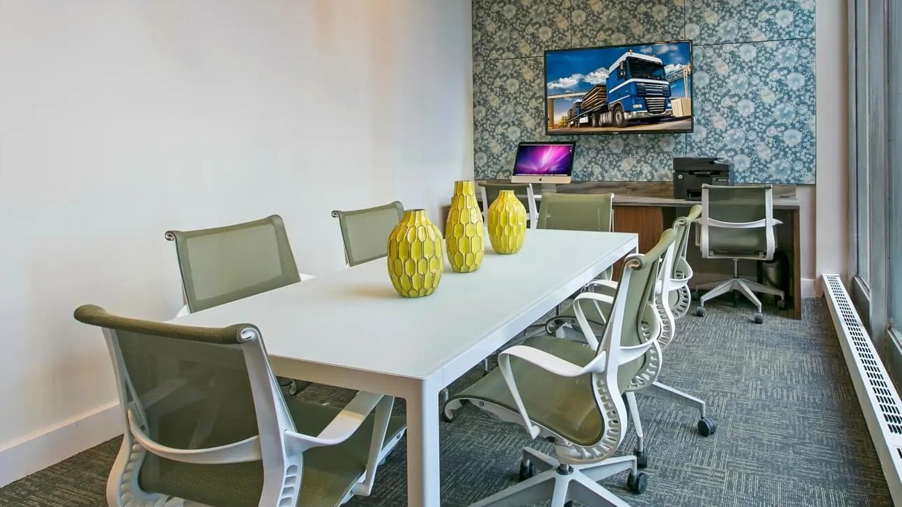 Bright coworking and conference room with long table, ergonomic chairs, and large window at 860 N Dewitt Apartments in Chicago