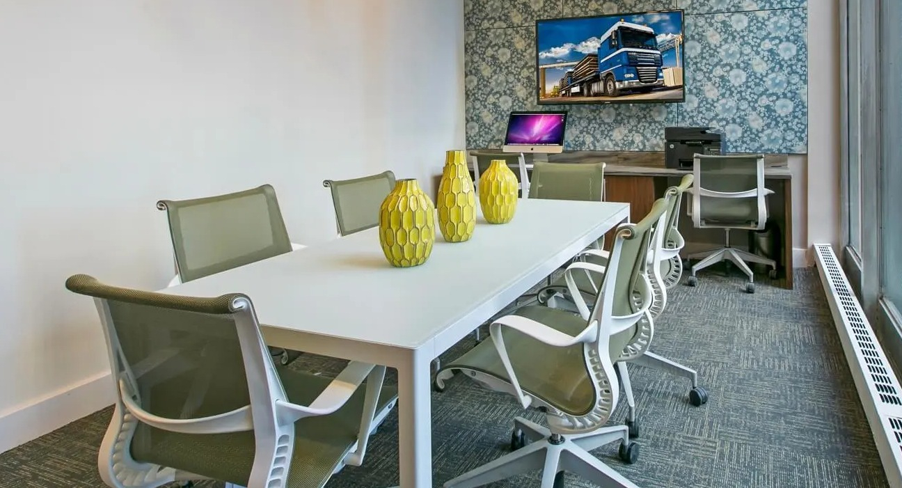 Bright coworking and conference room with long table, ergonomic chairs, and large window at 860 N Dewitt Apartments in Chicago