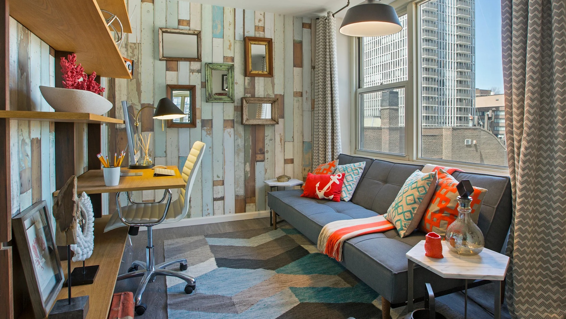 Cozy den or home office with built-in desk, floating shelves, patterned accent wall, and sofa by a window at 860 N Dewitt Apartments in Chicago