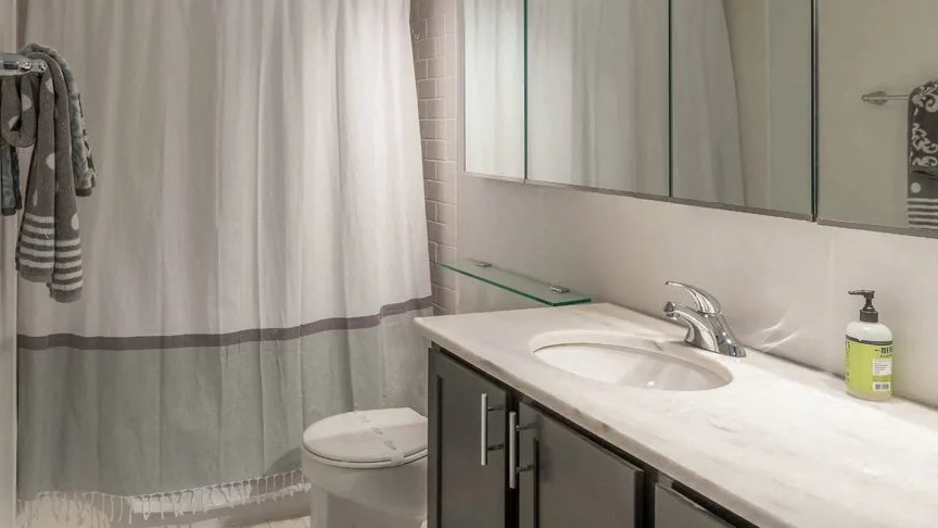 Contemporary bathroom with long vanity, mirrored cabinets, bright lighting, and a shower-tub with curtain at 860 N Dewitt Apartments in Chicago