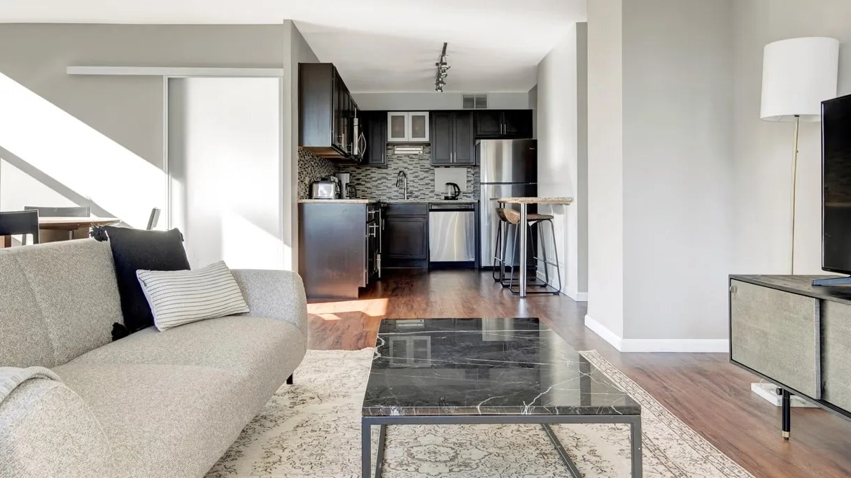 Modern living room with sunlit windows, black marble coffee table, and updated open kitchen with breakfast bar at 860 N Dewitt Apartments in Chicago
