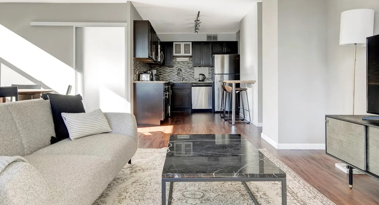 Modern living room with sunlit windows, black marble coffee table, and updated open kitchen with breakfast bar at 860 N Dewitt Apartments in Chicago