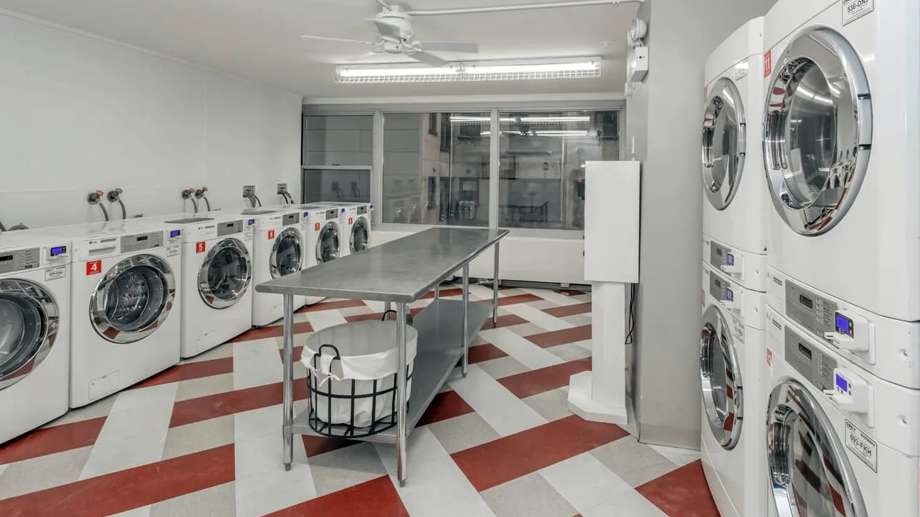 Bright on-site laundry room with multiple washers and dryers, folding table, and checkerboard floors at 860 N Dewitt Apartments in Chicago