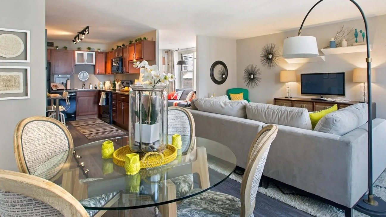Open-concept dining and living area with glass table, cozy sectional, and neutral tones leading to the kitchen at 860 N Dewitt Apartments in Chicago