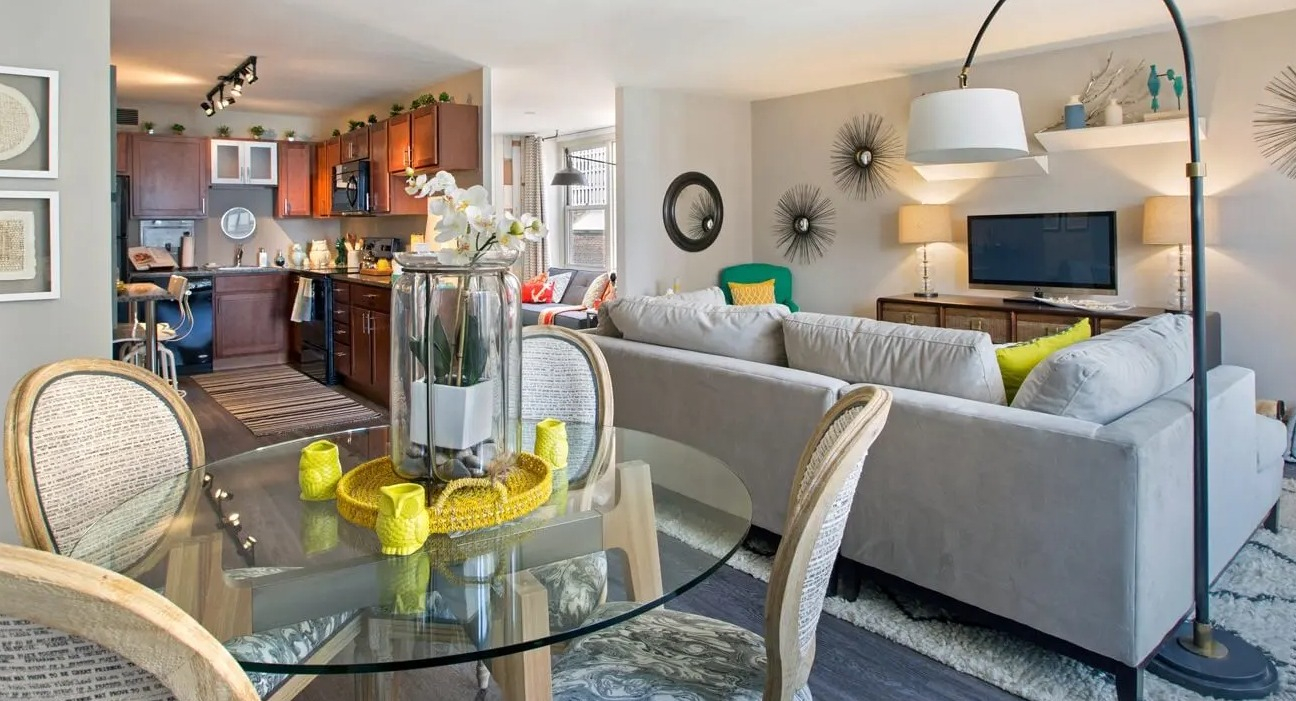 Open-concept dining and living area with glass table, cozy sectional, and neutral tones leading to the kitchen at 860 N Dewitt Apartments in Chicago
