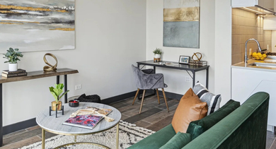 Cozy living area with green velvet sofa, round coffee table, compact kitchenette, and small work desk at Aberdeen East Apartments in Chicago