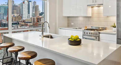 Modern white kitchen with quartz island, pendant lights, bar stools, stainless appliances, and impressive skyline views at Aberdeen East Apartments in Chicago