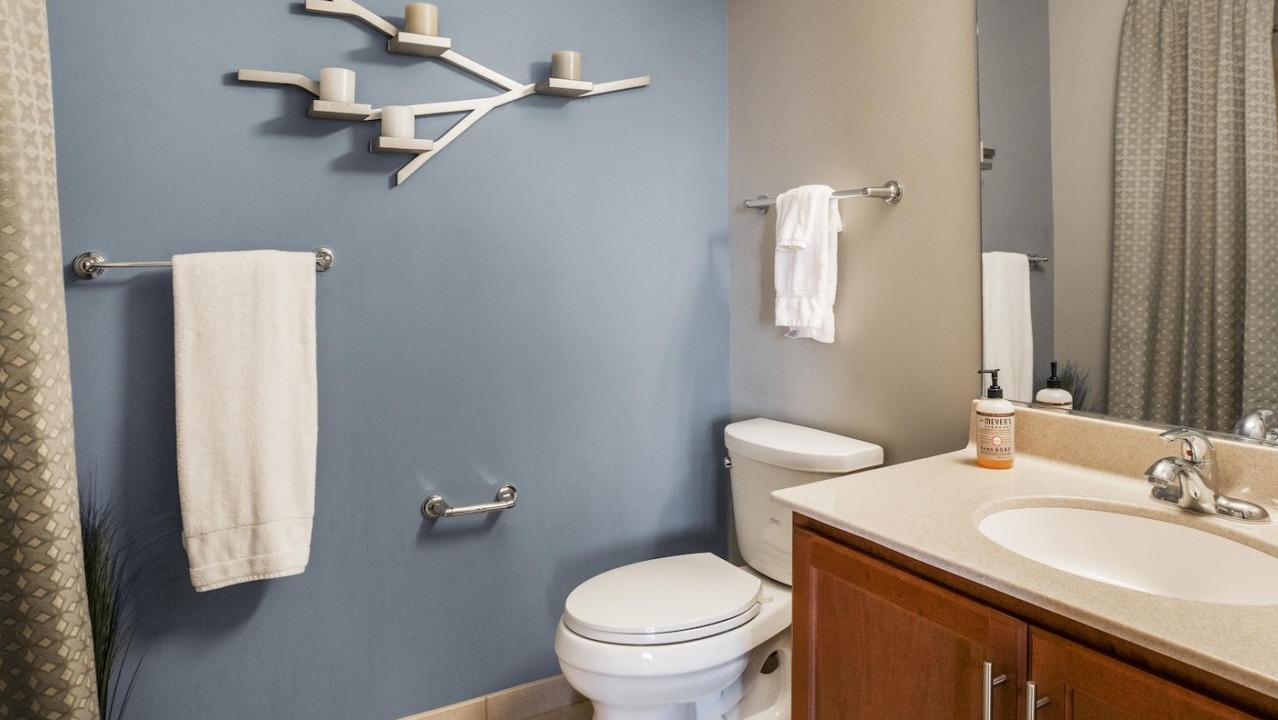 Contemporary bathroom at Alta at K Station in Chicago featuring a blue accent wall, sleek vanity, large mirror, and towel bars for a clean, modern look