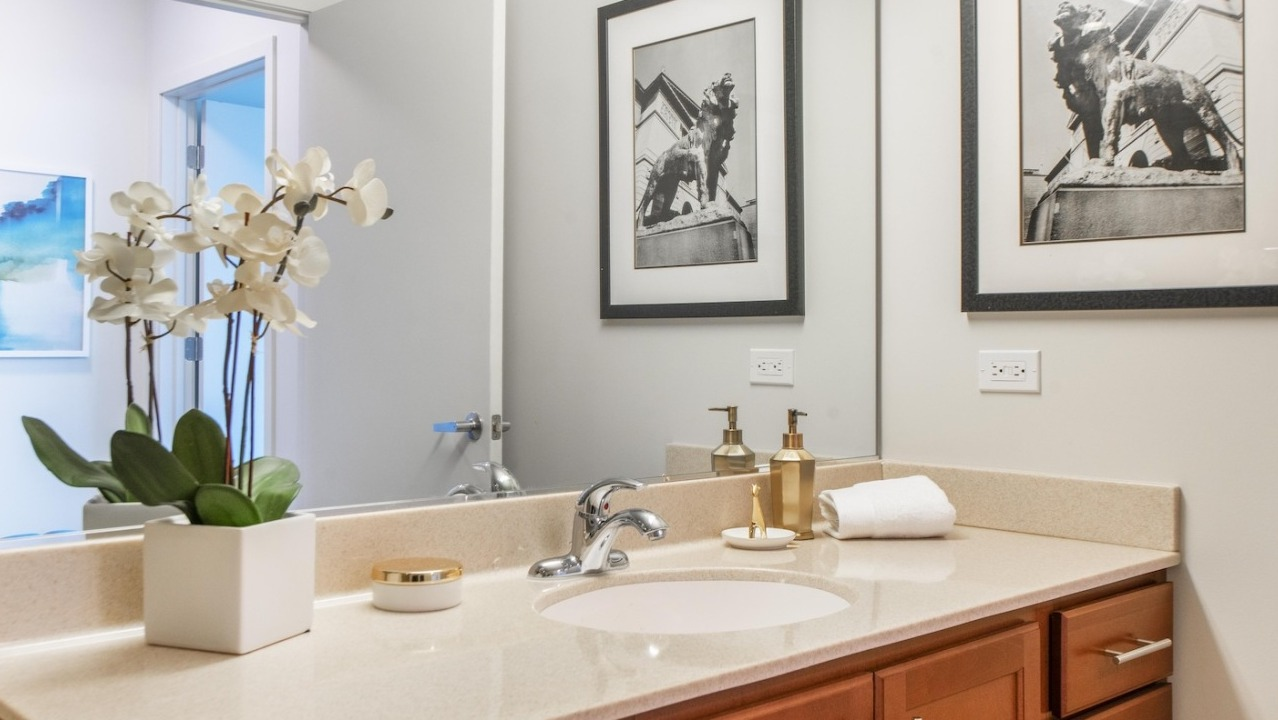 Bathroom at Alta at K Station with a sleek vanity, large mirror, neutral tones, and decorative orchid plant for a refined modern style