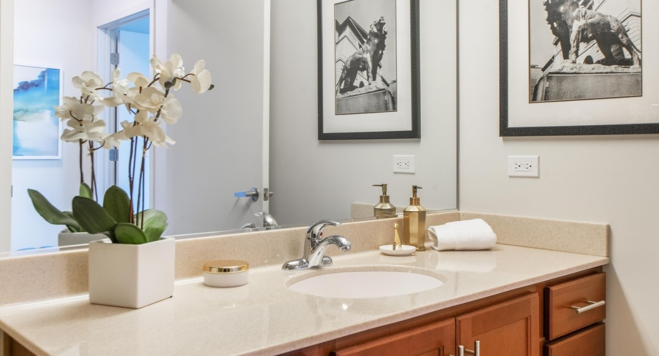 Bathroom at Alta at K Station with a sleek vanity, large mirror, neutral tones, and decorative orchid plant for a refined modern style