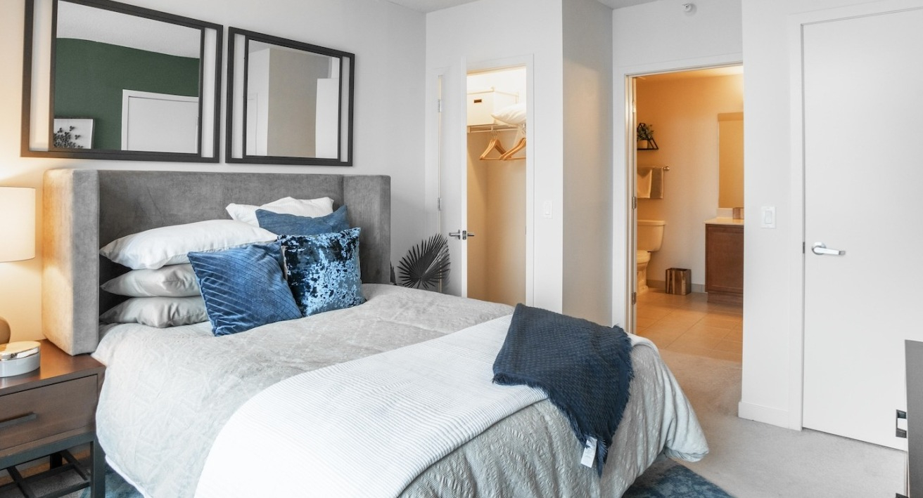Master bedroom at Alta at K Station with plush headboard, layered pillows, warm lighting, and direct access to an ensuite bath and walk-in closet