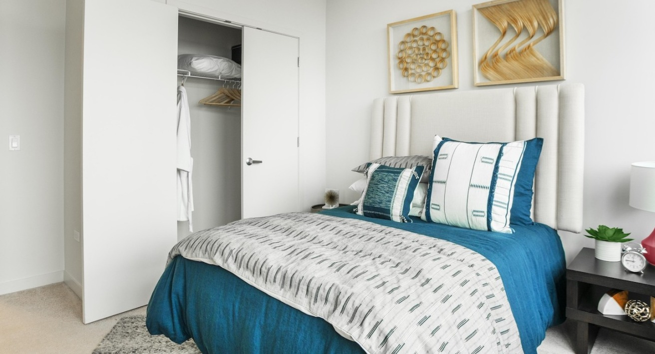 Modern bedroom at Alta at K Station in Chicago featuring a bright interior, upholstered headboard, bold blue bedding, and wall art above the bed