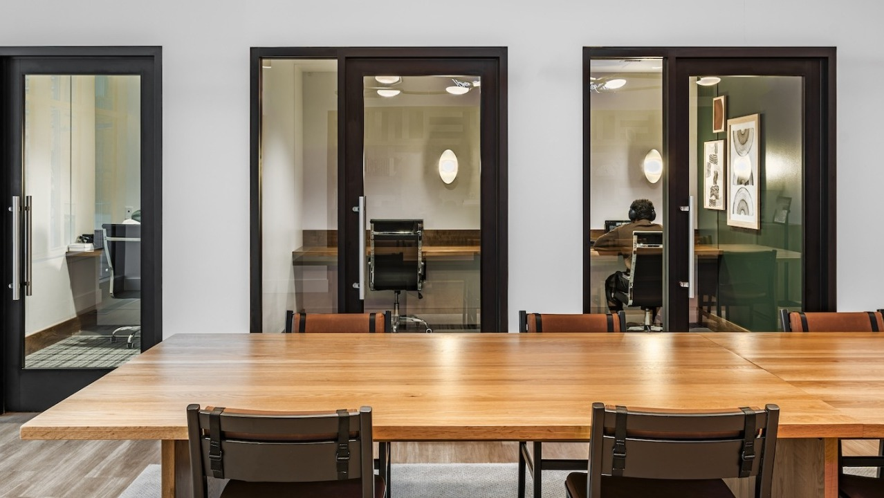 Coworking and conference rooms at Alta at K Station featuring private glass offices and a large communal table, ideal for remote work and meetings