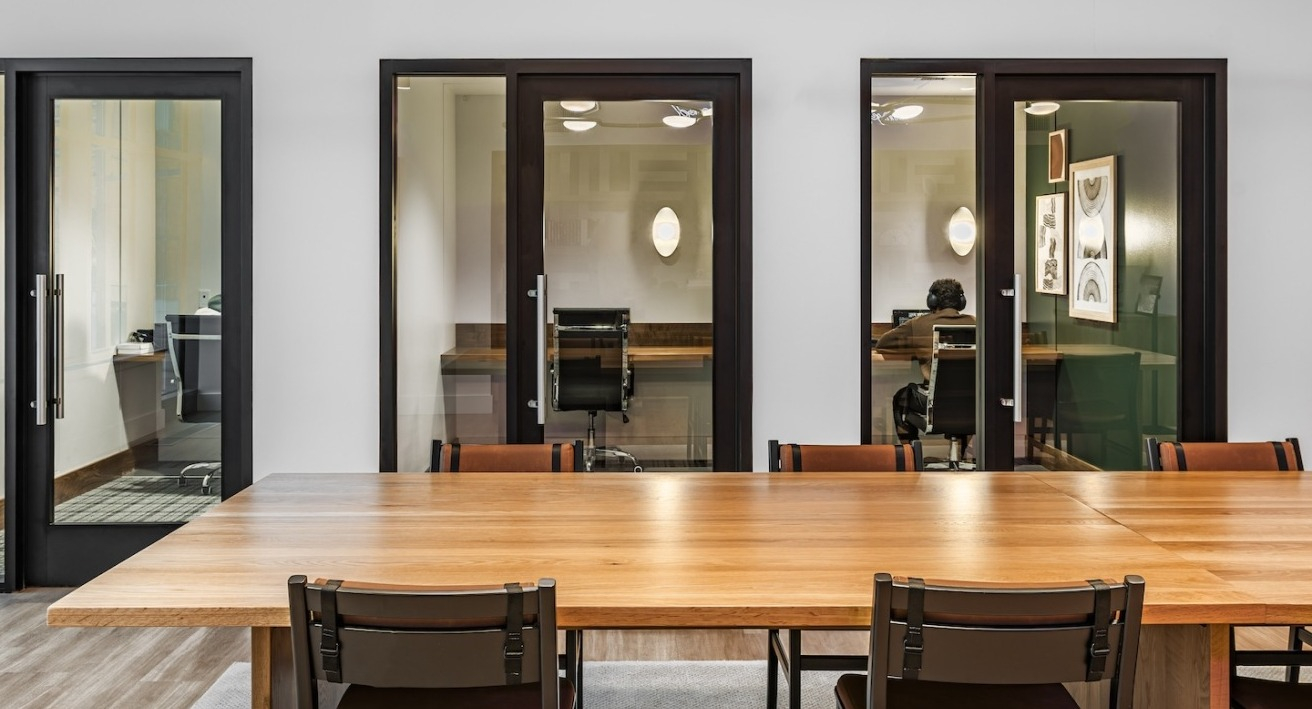 Coworking and conference rooms at Alta at K Station featuring private glass offices and a large communal table, ideal for remote work and meetings
