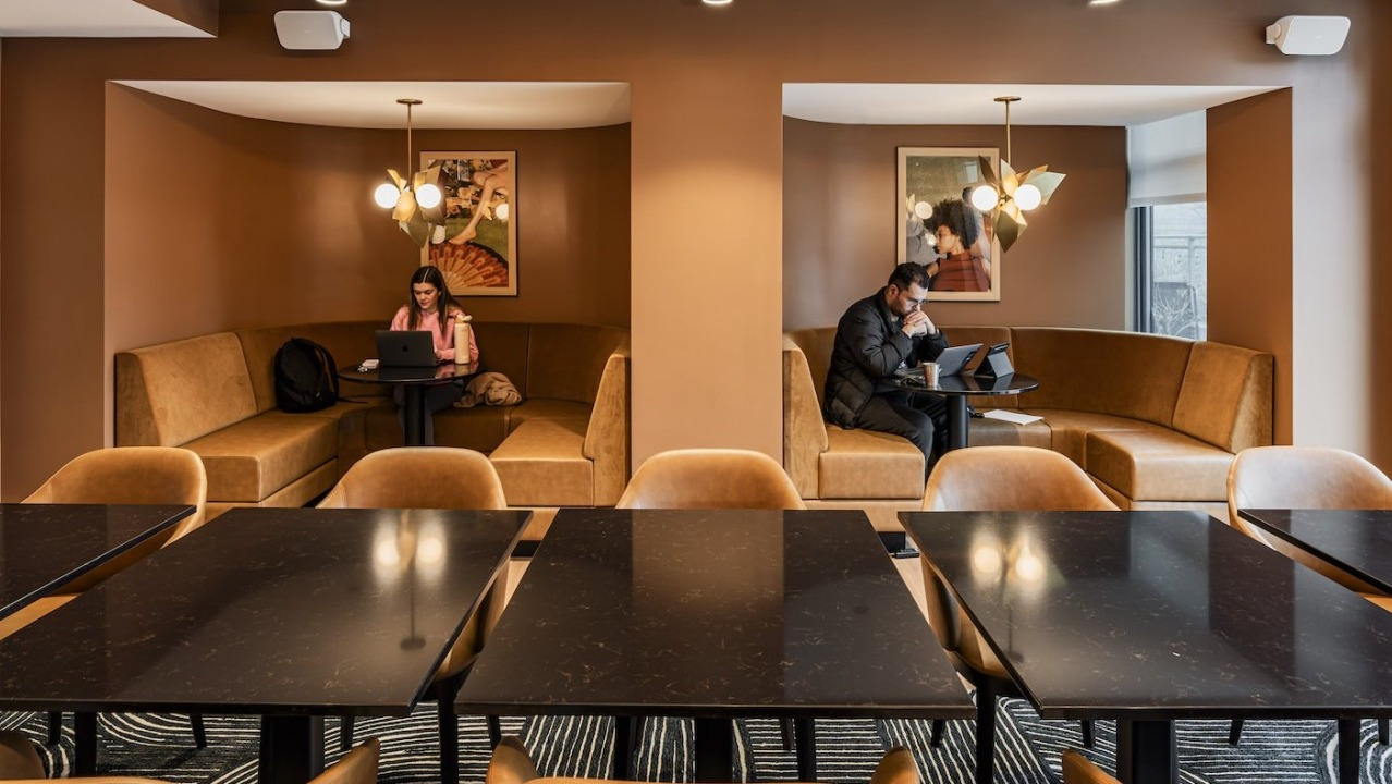 Coworking lounge at Alta at K Station with warm-toned walls, cozy private booths, modern lighting, and residents working on laptops