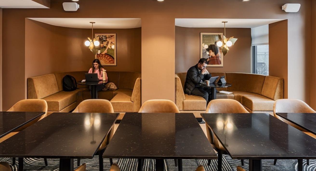 Coworking lounge at Alta at K Station with warm-toned walls, cozy private booths, modern lighting, and residents working on laptops