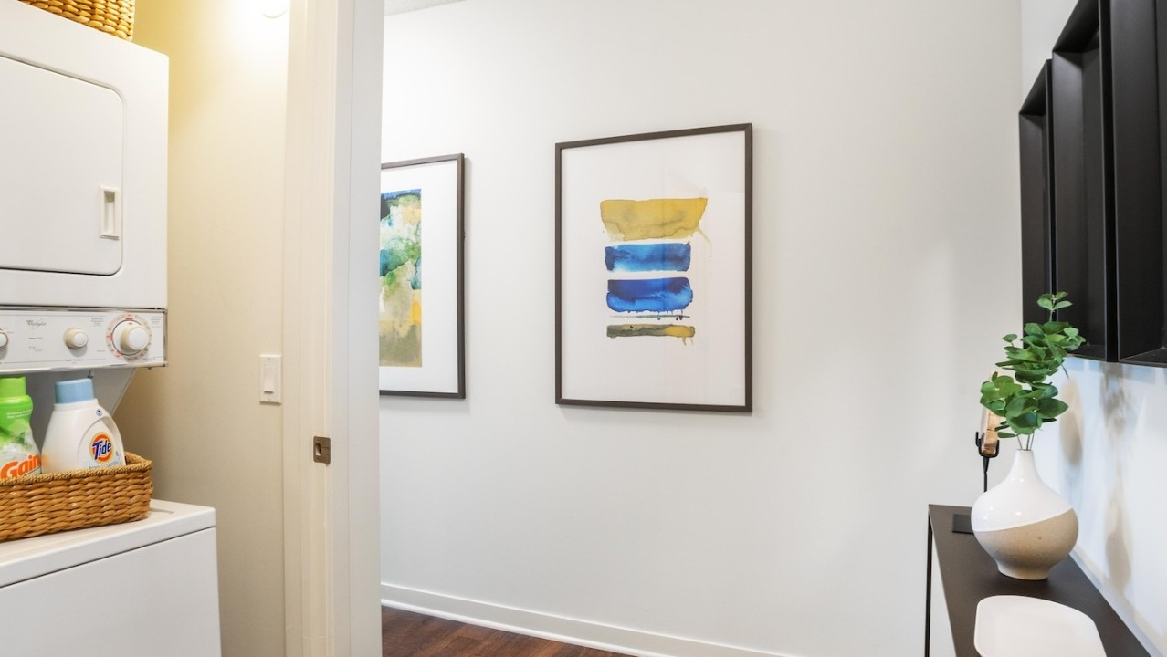 Entrance hallway at Alta at K Station featuring in-unit washer and dryer, wood floors, modern wall art, and a slim console table for practical style