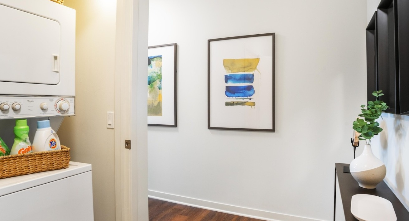 Entrance hallway at Alta at K Station featuring in-unit washer and dryer, wood floors, modern wall art, and a slim console table for practical style