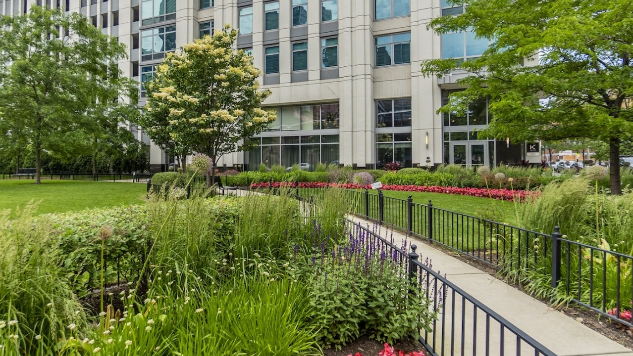 Alta at K Station exterior with landscaped garden, flowering plants, manicured lawn, and pathway lined with greenery and flowers