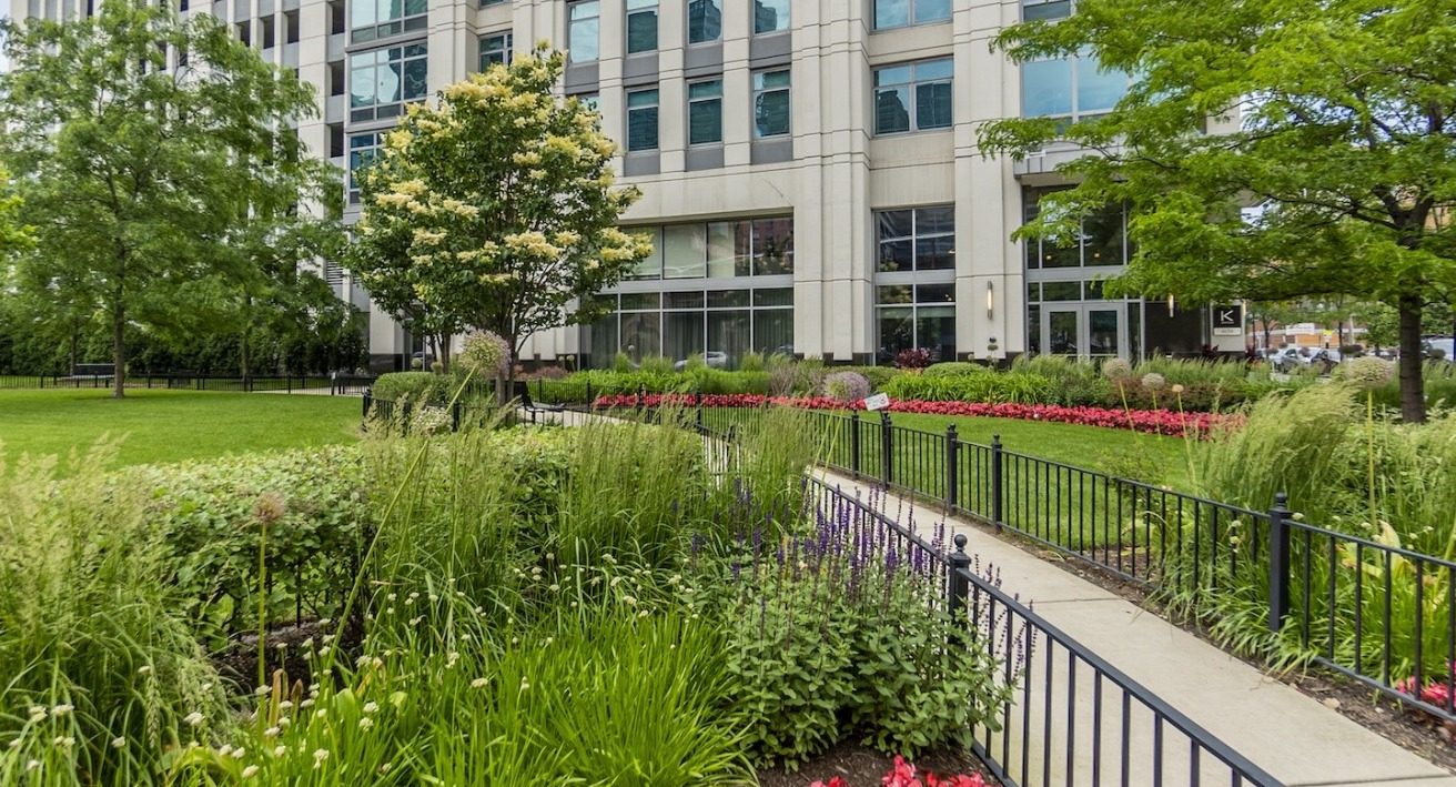 Alta at K Station exterior with landscaped garden, flowering plants, manicured lawn, and pathway lined with greenery and flowers